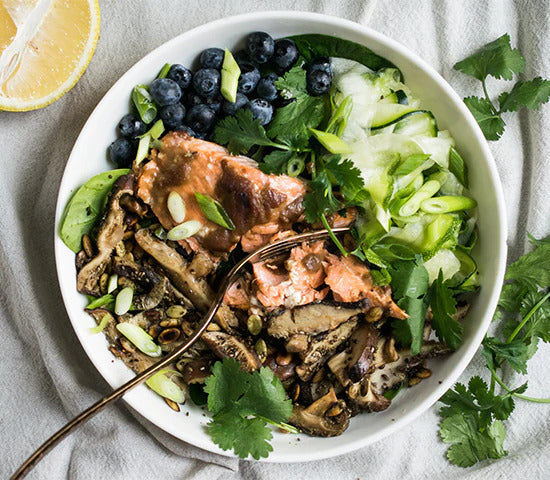 Bowl of greens topped with teriyaki salmon and sprinkled with Navitas Organics Hemp Seeds