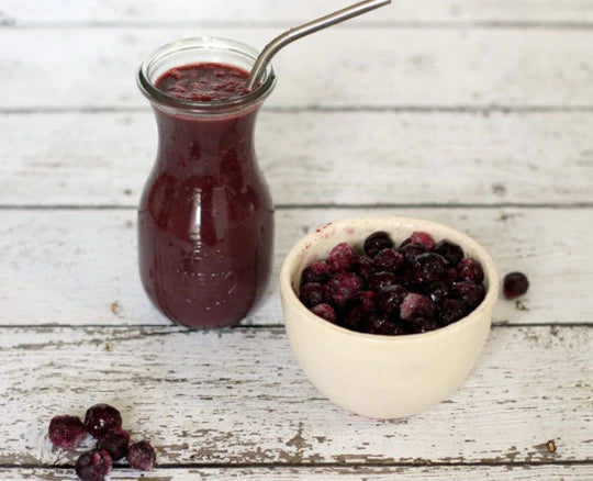 Dark berry superfood smoothie next to a bowl of whole, fresh berries