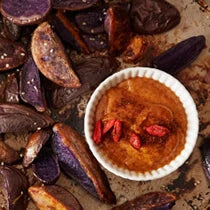 Baking sheet spread with purple potato wedge fries and served with a spicy goji aioli