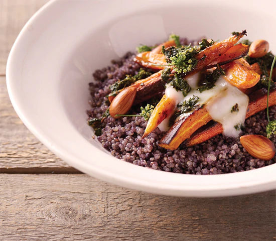 Bowl of purple quinoa topped with roasted carrots and drizzled in coconut sauce
