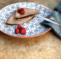 Plate with two banana crepes filled with a cacao butter spread and topped with strawberries