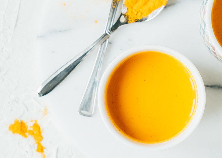 A turmeric latte made with Navitas Organics Turmeric Powder in a white ceramic mug next to spoons of turmeric powder