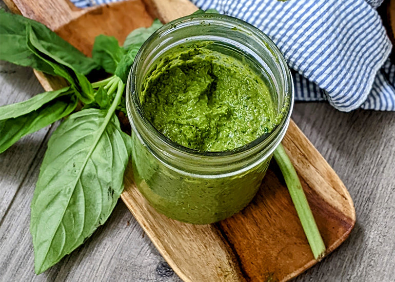 Pesto sauce made with Navitas Organics Superfood+ Greens Blend, Wheatgrass Powder and Hemp Seeds in a glass jar on a wooden board with basil leaves