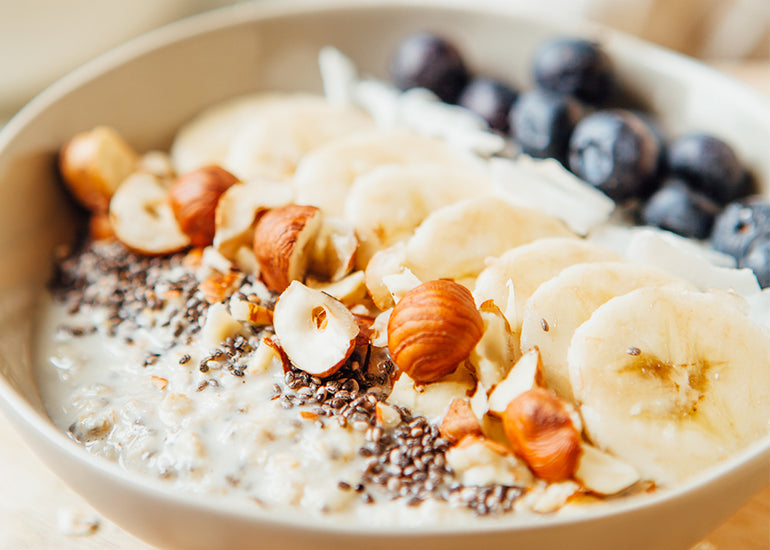 A bowl of overnight oats made with Navitas Organics Chia Seeds, topped with hazelnuts, banana slices, coconut flakes and blueberries