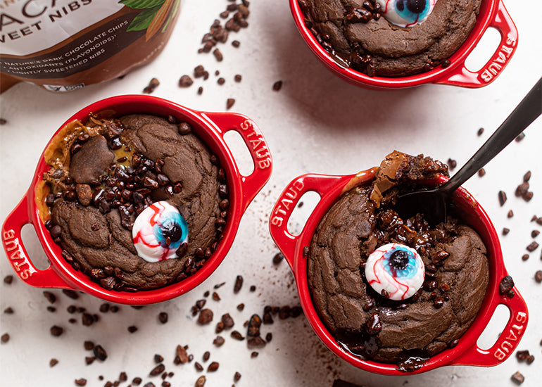 Mini chocolate cakes made with Navitas Organics Cacao Powder in ceramic baking dishes, decorated with candy eyeballs and Navitas Organics Cacao Sweet Nibs