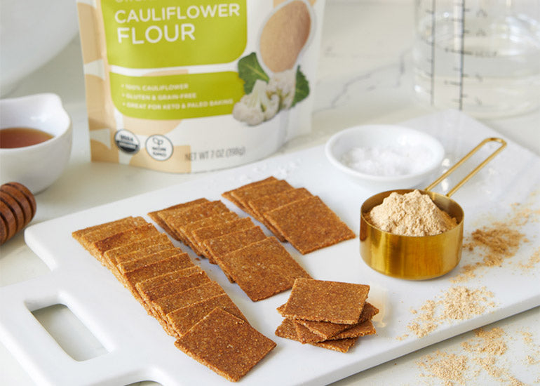 A cutting board topped with rows of cauliflower crackers made with Navitas Organics Cauliflower Flour