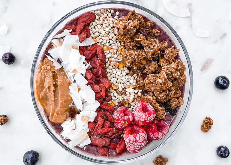 An acai bowl made with Navitas Organics Acai Powder, Cacao+ Antioxidant Blend, Chia Seeds and Hemp Seeds, topped with granola, coconut flakes, nut butter and Navitas Organics Goji Berries