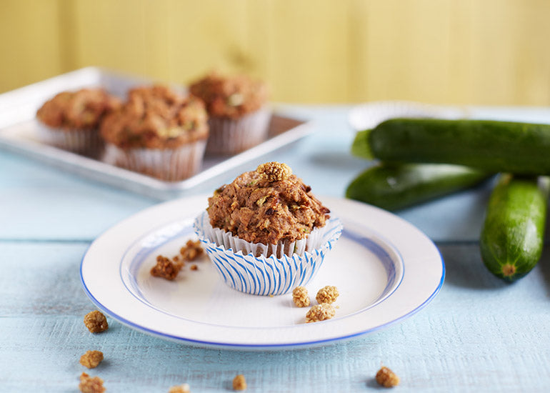 A muffin made with Navitas Organics Chia Powder and Mulberries sitting on a plate surrounded by zucchinis and mulberries