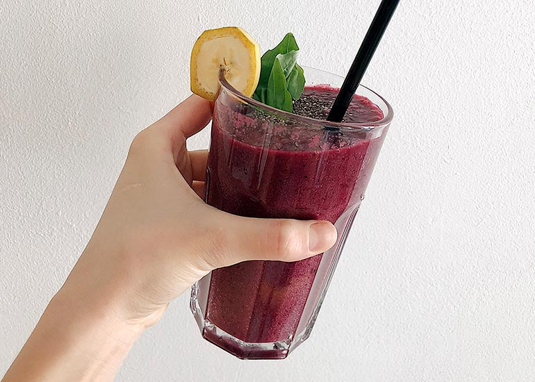 A woman holding a glass filled with a purple smoothie made with Navitas Organics Acai Powder and Chia Powder, garnished with Navitas Organics Chia Seeds