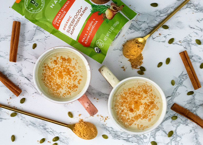 Two mugs filled with lattes made with Navitas Organics Superfood+ Adaptogen Blend, garnished with cinnamon, cardamom and nutmeg