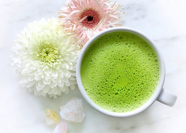 A matcha latte made with Navitas Organics Matcha Powder and Maca Powder in a ceramic mug surrounded by flowers and crystals.