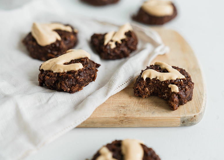 A cutting board topped with a linen napkin and several cacao peanut butter cookies made with Navitas Organics Cacao Powder, drizzled with a peanut butter topping.