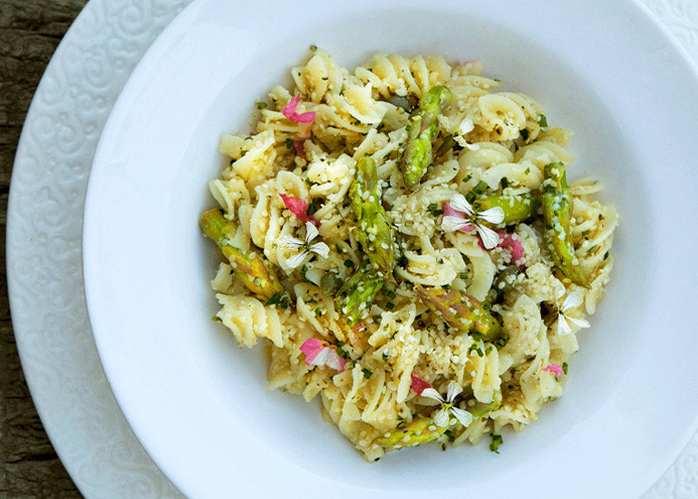 A bowl of pasta mixed with asparagus, topped with a cream sauce made with Navitas Organics Cashew Nuts, and sprinkled with Navitas Organics Hemp Seeds.
