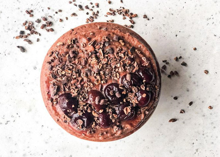 A chocolate cherry smoothie bowl made with Navitas Organics Cacao Powder and Superfood+ Adaptogen Blend, topped with Navitas Organics Cacao Nibs and cherries.