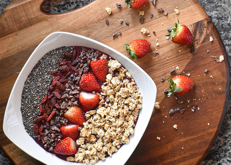 A cacao acai berry bowl made with Navitas Organics Cacao+ Antioxidant Blend, topped with fresh strawberries, granola, and Navitas Organics Goji Berries, Cacao Nibs and Chia Seeds.