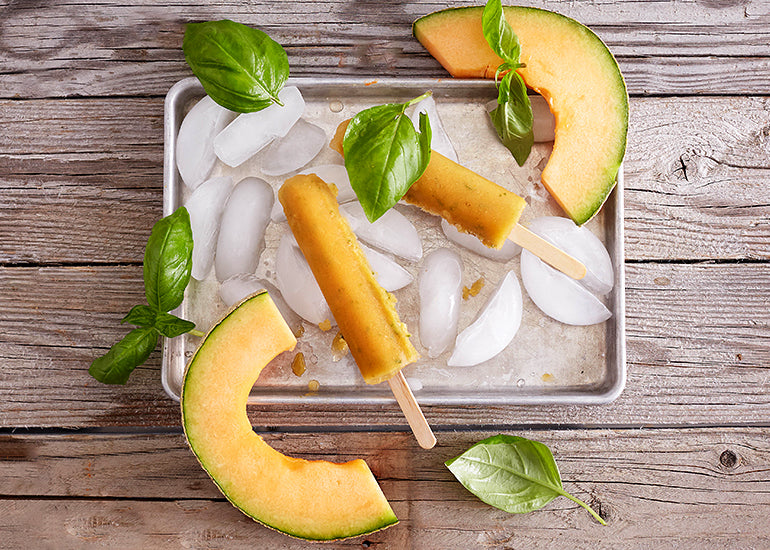 A pan filled with ice, topped with cantaloupe basil ice pops made with Navitas Organics Camu Powder and fresh cantaloupe slices.