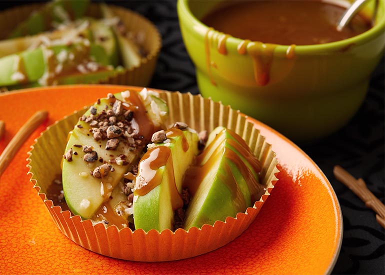 A cupcake wrapper filled with caramel apple superfood nachos, topped with Navitas Organics Cacao Sweet Nibs and Hemp Seeds.