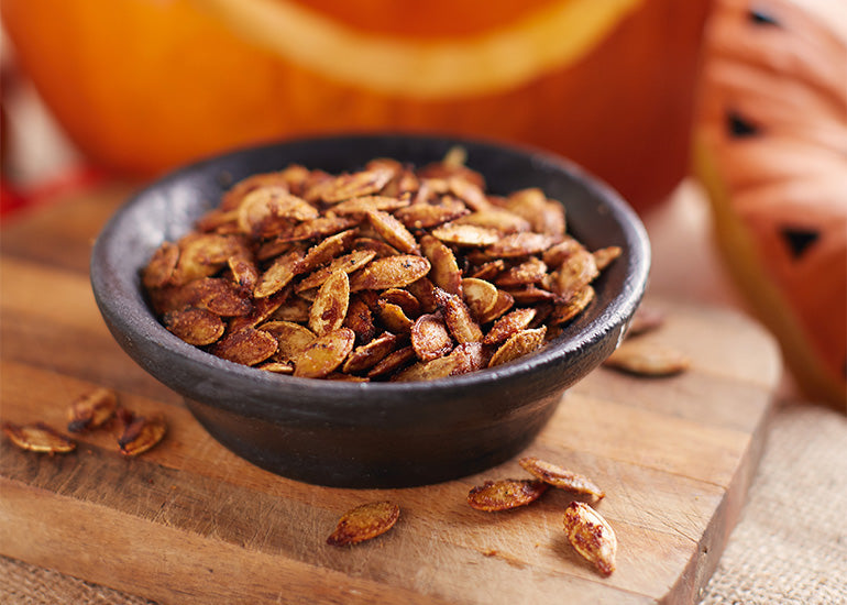 A dish filled with pumpkin seeds coated with a sweet seasoning made with Navitas Organics Maca Powder.