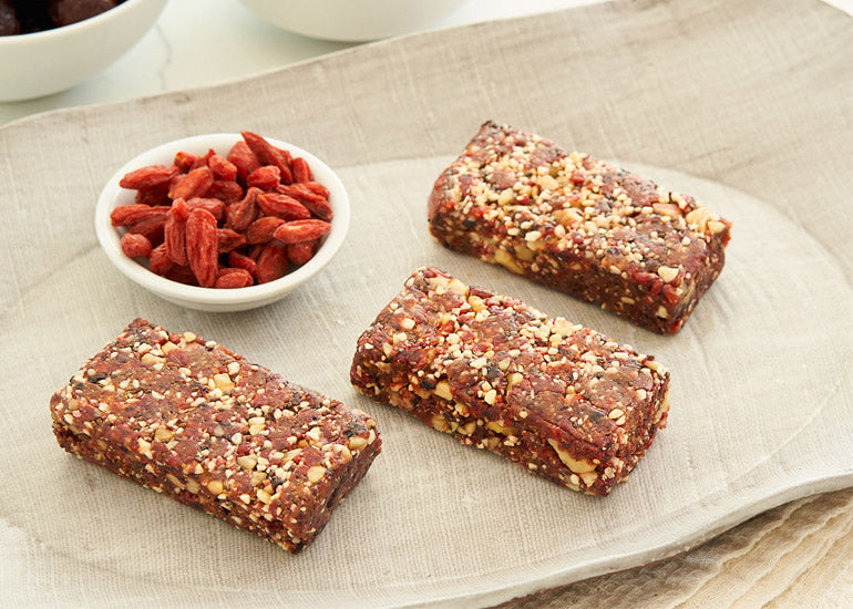 A row of cherry goji bars made with Navitas Organics Goji Berries and Chia Seeds aside a small dish filled with Navitas Organics Goji Berries.