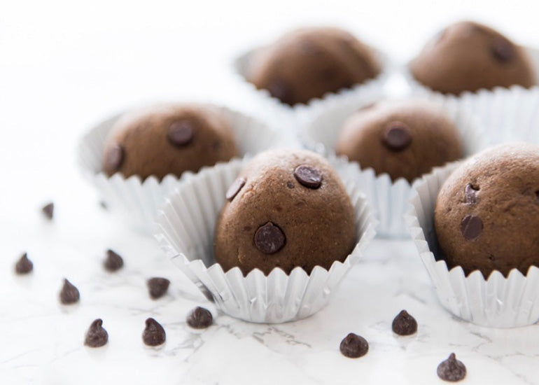Chocolate chip brownie bites made with Navitas Organics Cacao & Greens Essential Blend Protein Powder and Cashew Nuts, sitting in paper wrappers.
