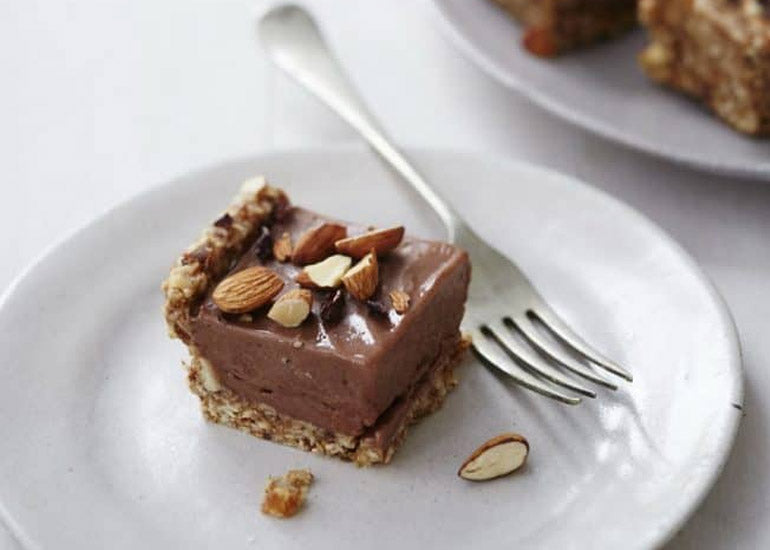 A slice of chocolate coconut banana tart made with Navitas Organics Cacao Powder and Cacao Nibs, topped with almonds, on a plate with a fork.