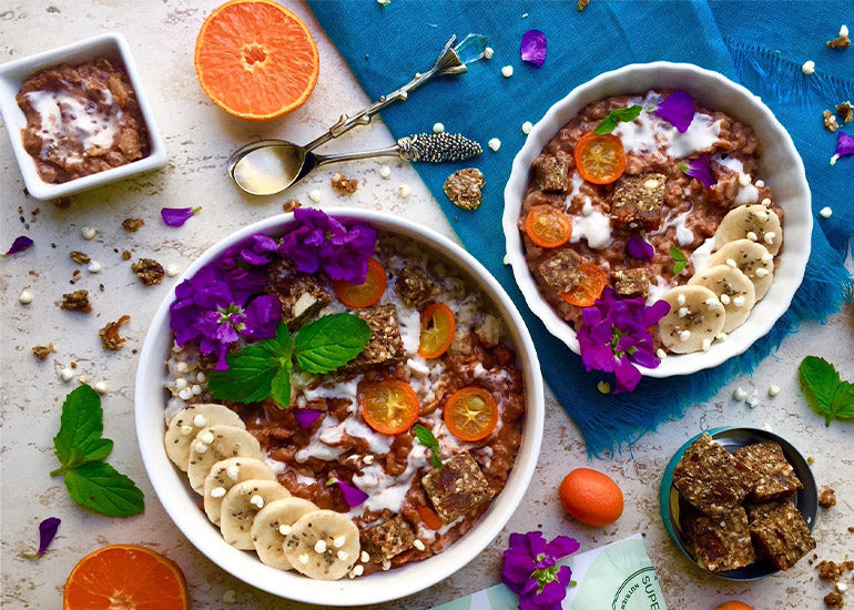 Two bowls filled with chocolate coconut chia pudding oats made with Navitas Organics Chia Seeds, Cacao Powder and Superfood+ Adaptogen Blend, topped with sliced bananas and Navitas Organics Power Snacks.