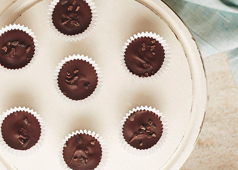 A plate of chocolate peanut butter protein cups made with Navitas Organics Cacao Butter, Cacao Powder and Cacao Sweet Nibs.