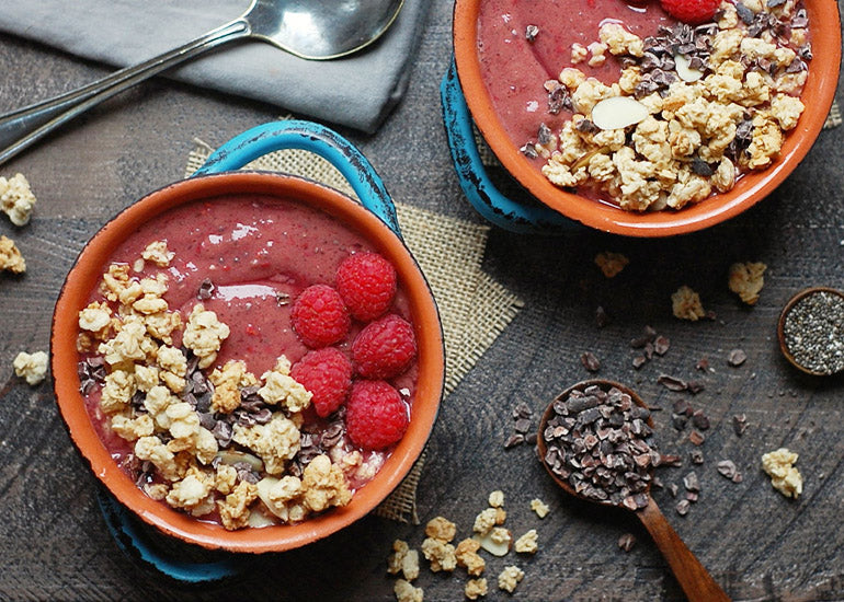 Chocolate raspberry smoothie bowls made with Navitas Organics Cacao Powder and Chia Seeds, topped with gluten-free granola, fresh raspberries and Navitas Organics Cacao Nibs.