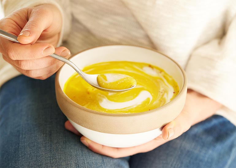 A woman holding a bowl of creamy yellow soup made with Navitas Organics Turmeric Powder.