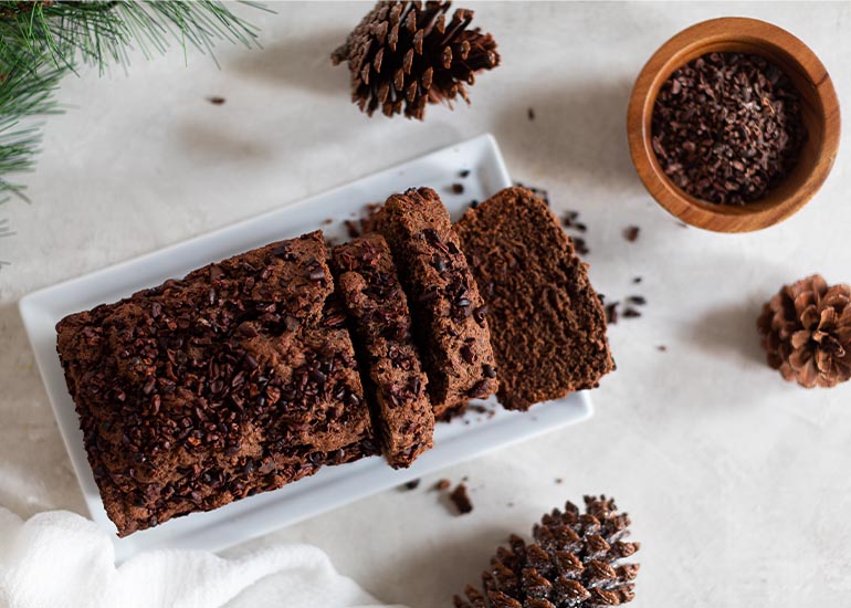 A loaf of chocolate bread made with Navitas Organics Cacao Powder and Cacao Sweet Nibs, sliced on a plate.
