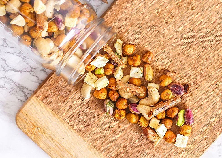 A mason jar filled with trail mix made with Navitas Organics Turmeric Powder and Cashew Nuts, spilling out over a cutting board.
