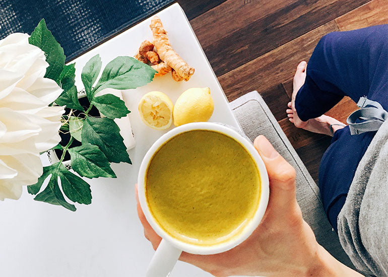 A woman holding a turmeric latte made with Navitas Organics Turmeric Powder and Camu Powder.