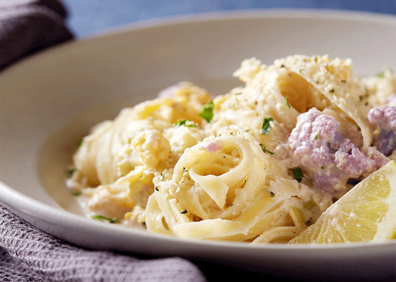 A bowl of fettuccine pasta made with Navitas Organics Cashew Nuts, mixed with vegetables and spices, topped with Navitas Organics Hemp Seeds.