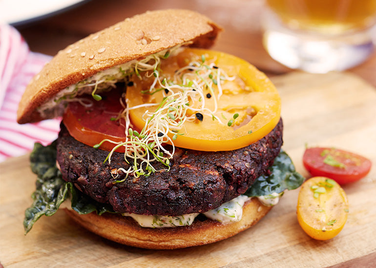 A lentil beet burger made with Navitas Organics Chia Powder and Hemp Seeds on a bun, topped with sliced tomato and sprouts.