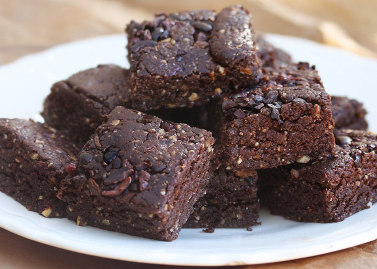 A plate piled high with no-bake fudge brownies made with Navitas Organics Cacao Powder and Cacao Nibs.