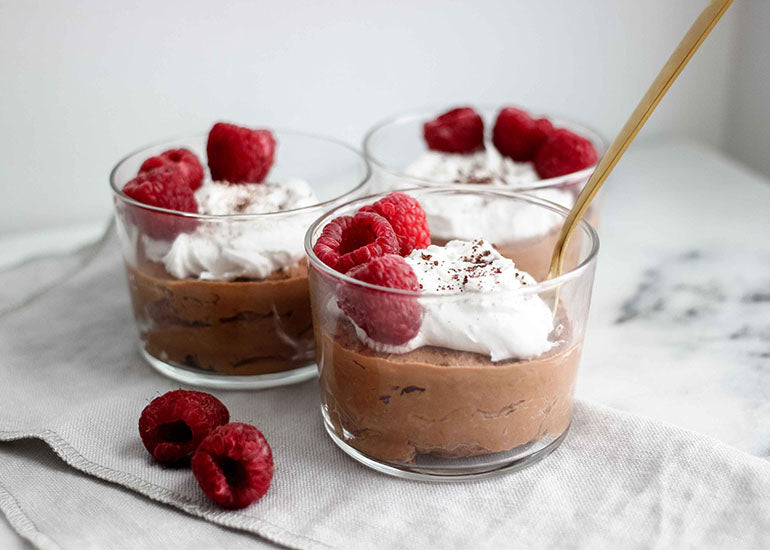 Three glass dishes filled with a chocolate mousse made with Navitas Organics Cacao Powder, Maca Powder and Cacao Nibs, topped with whipped cream and fresh raspberries.