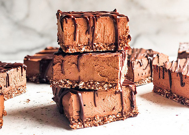 A stack of chocolate cheesecake bars made with Navitas Organics Cacao Powder and Cacao Wafers, drizzled with melted chocolate.