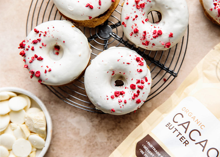 White chocolate raspberry donuts made with Navitas Organics Cacao Butter on a cooling rack.