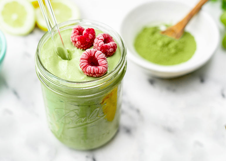A matcha pineapple smoothie made with Navitas Organics Matcha Powder in a mason jar topped with frozen raspberries.