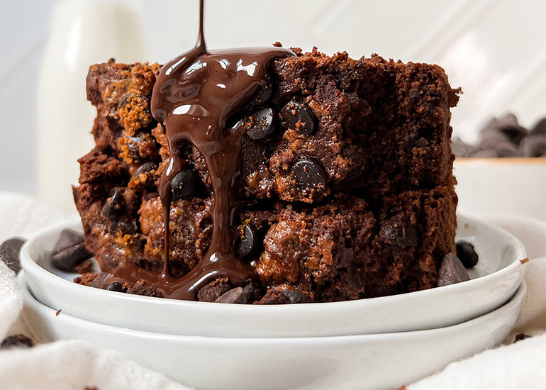 Chocolate pumpkin bread made with Navitas Organics Cacao Powder stacked on a plate with chocolate sauce being drizzled on top.