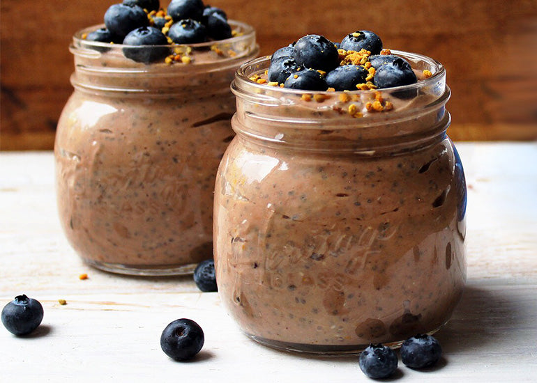 Two chocolate chia pudding cups made with Navitas Organics Cacao Powder and Chia Seeds in mason jars topped with blueberries and bee pollen. 