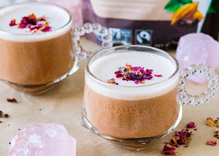 Two glass mugs filled with hot cocoa made with Navitas Organics Cacao Powder and Maca Powder, topped with rose petals.