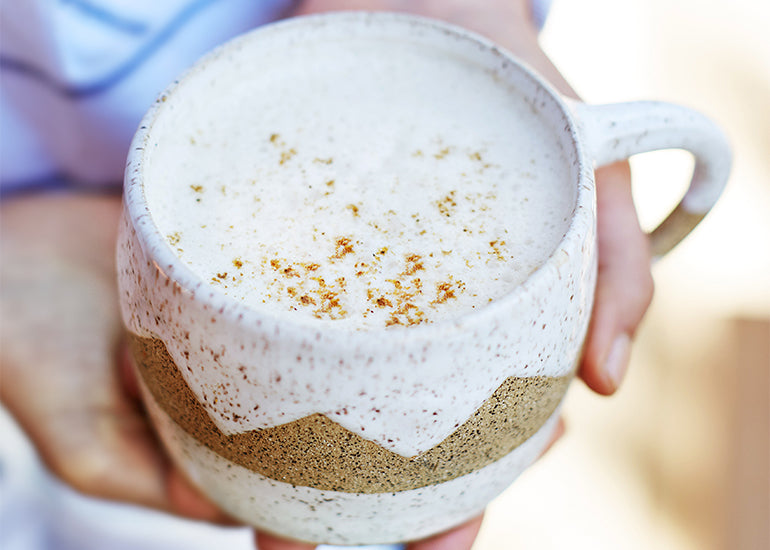 A woman holding a mug filled with a latte made with Navitas Organics Maca Powder