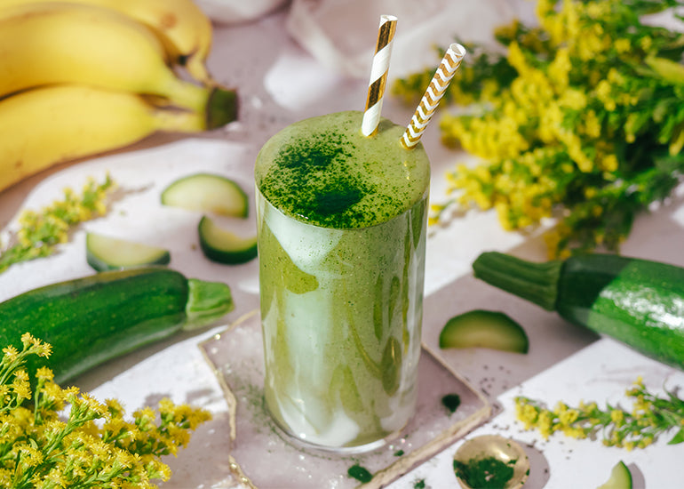 A green smoothie made with Navitas Organics Superfood+ Adaptogen Blend, Wheatgrass Powder and Superfood+ Greens Blend in a tall glass with straws.