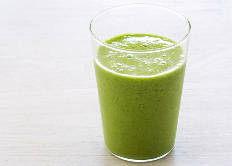 A glass filled with a green smoothie made with Navitas Organics Wheatgrass Powder.