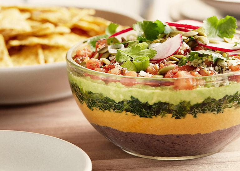 A bowl of seven-layer dip made with Navitas Organics Chia Seeds, Hemp Seeds and Wheatgrass Powder.