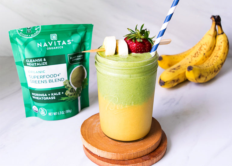 A layered smoothie made with Navitas Organics Turmeric Powder, Camu Powder and Superfood+ Greens Blend, topped with fresh banana slices and strawberries.