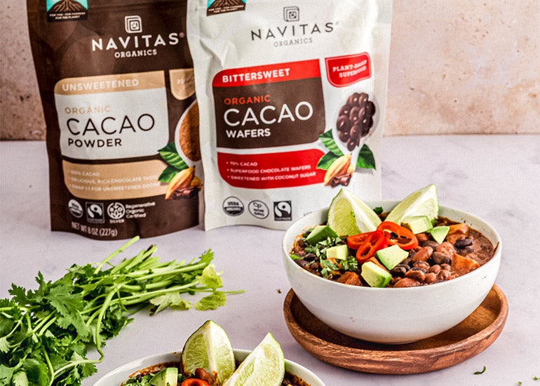Bowls of vegan cacao chili made with Navitas Organics Cacao Powder and Bittersweet Cacao Wafers, topped with cilantro, avocado, peppers, and lime.