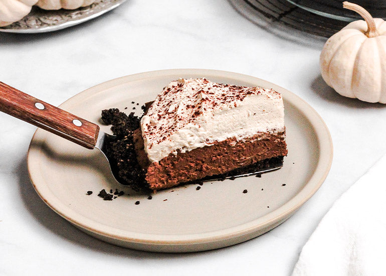 A slice of no-bake chocolate pie with pumpkin spice whipped cream made with Navitas Organics Cacao Powder and sweetened Cacao Wafers.