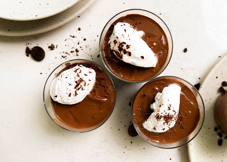 Three glasses filled with vegan chocolate mousse made with Navitas Organics Bittersweet Cacao Wafers, topped with coconut yogurt and shaved chocolate.